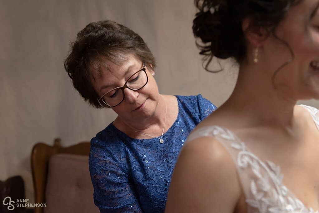 The mother of the bride assists her daughter with getting into her wedding dress.