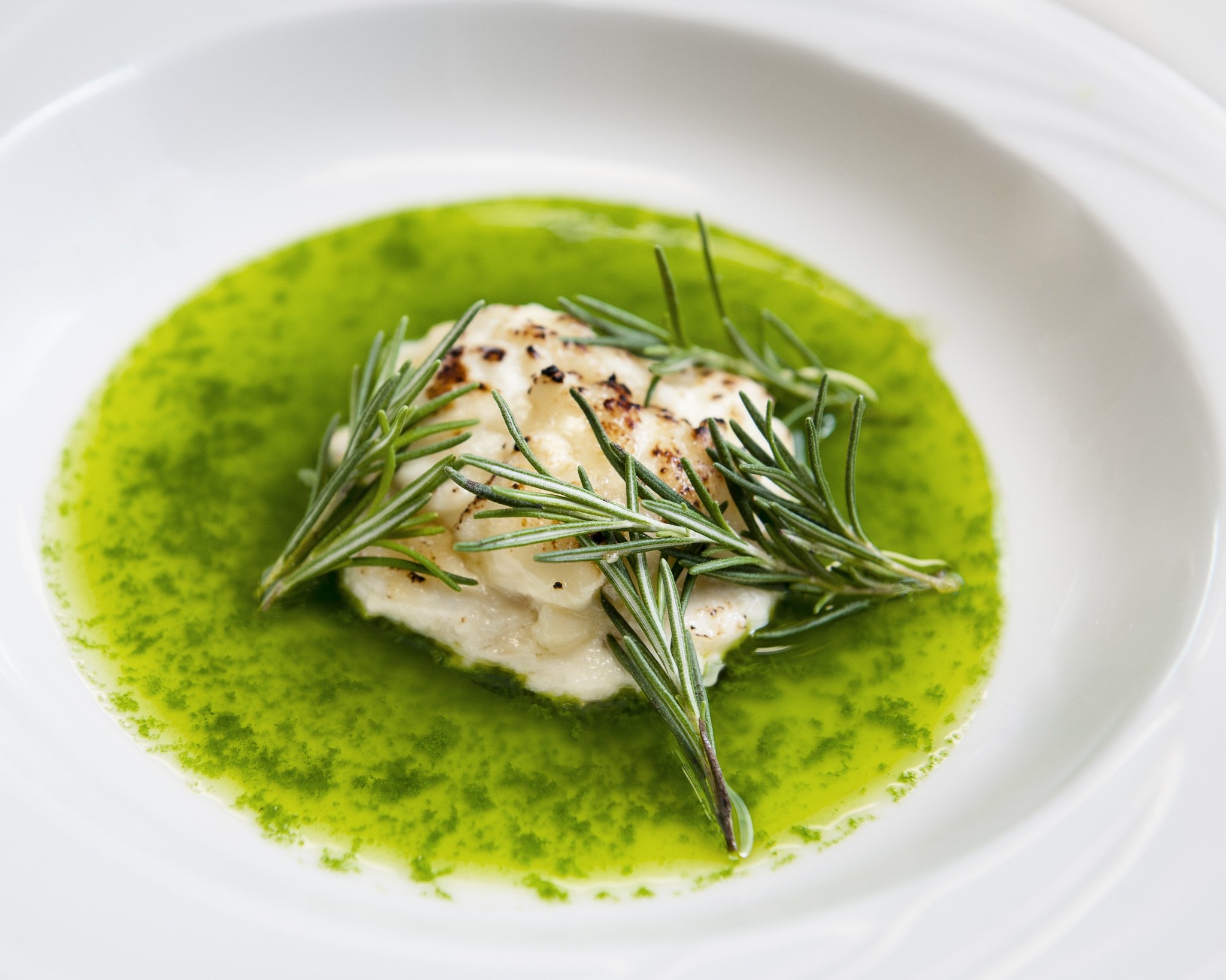 A ravioli plated with rosemary and pesto sauce.