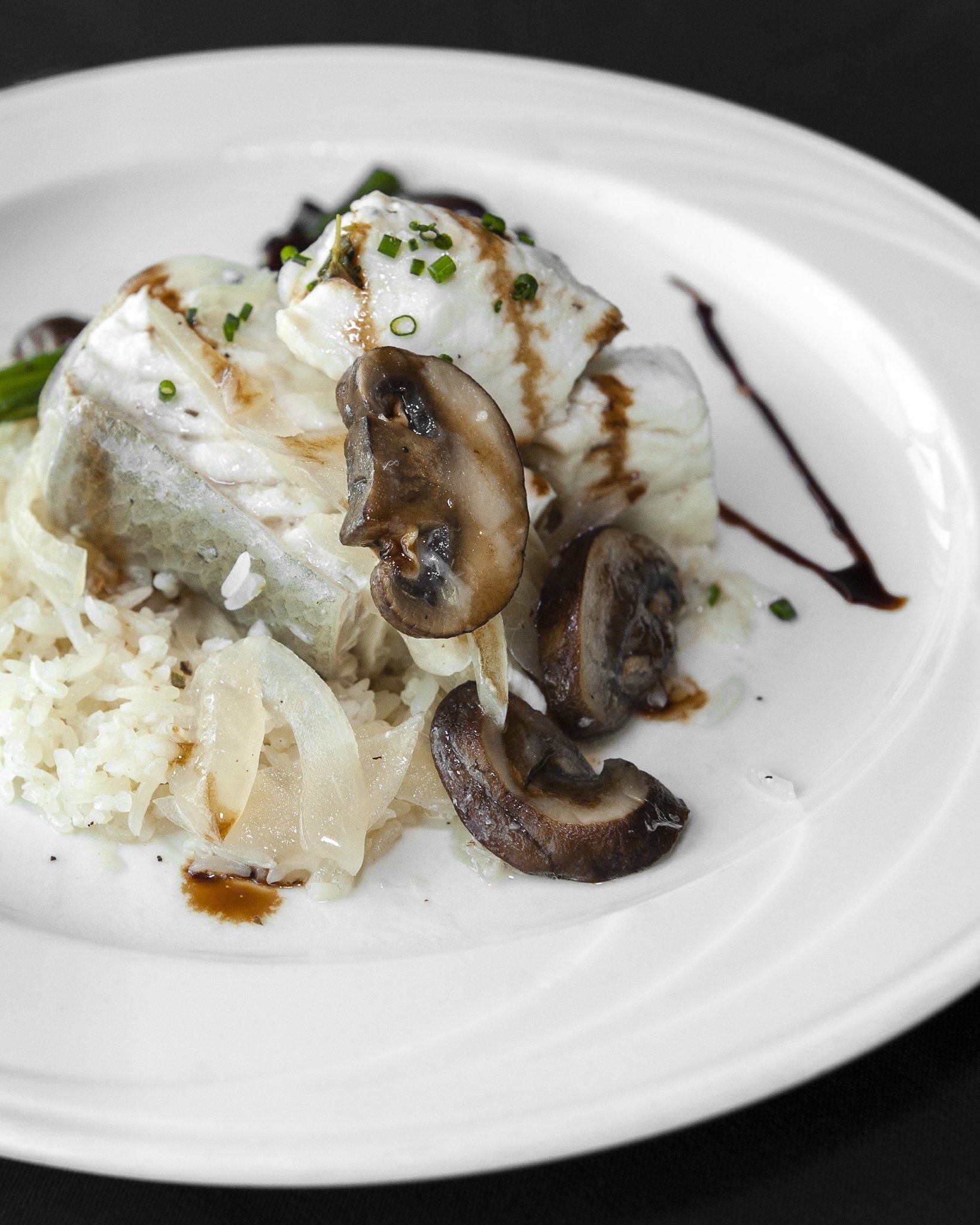 Close up of a mushroom on a plated dish of halibut with rice.