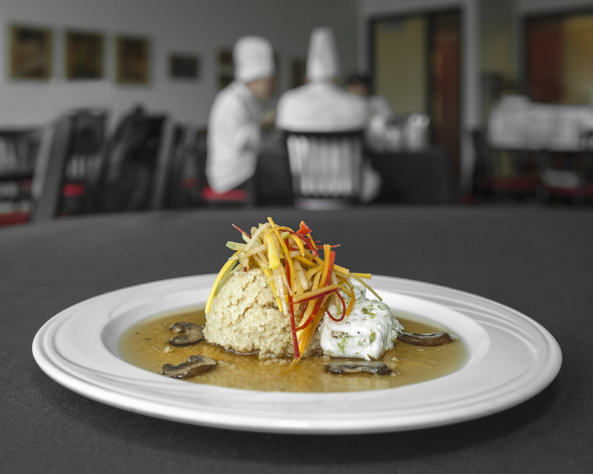 Close up of a prepared plate of halibut with culinary judges blurred in a background.