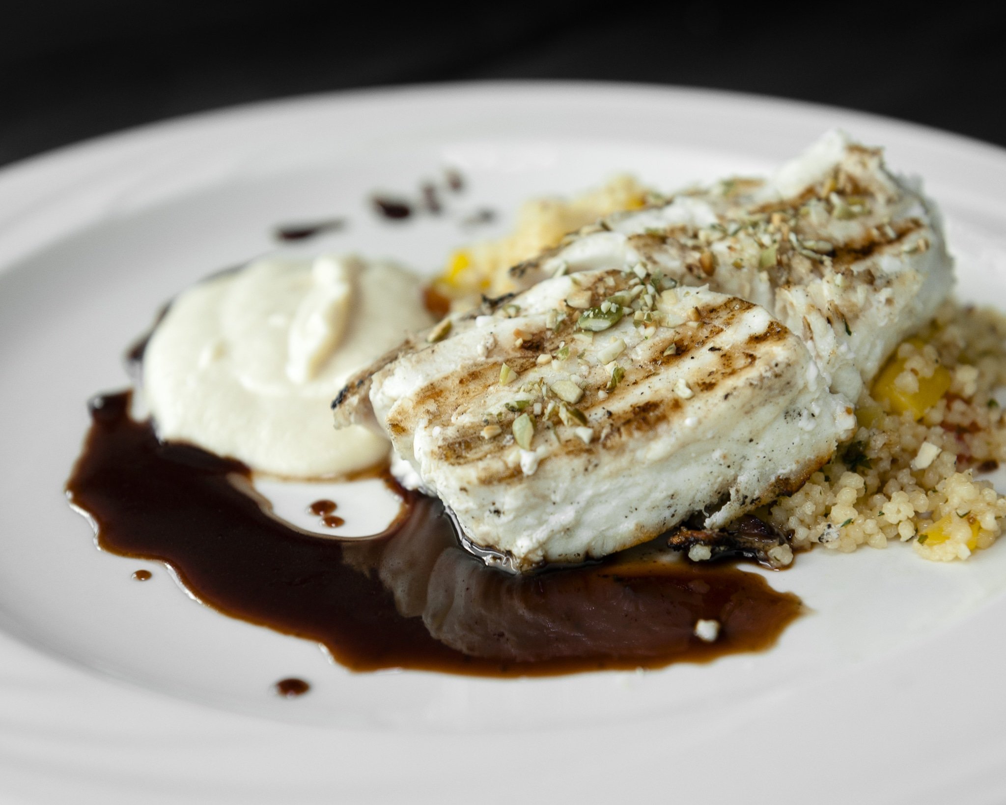 Halibut on a white plate with couscous, vegetable puree and nuts.