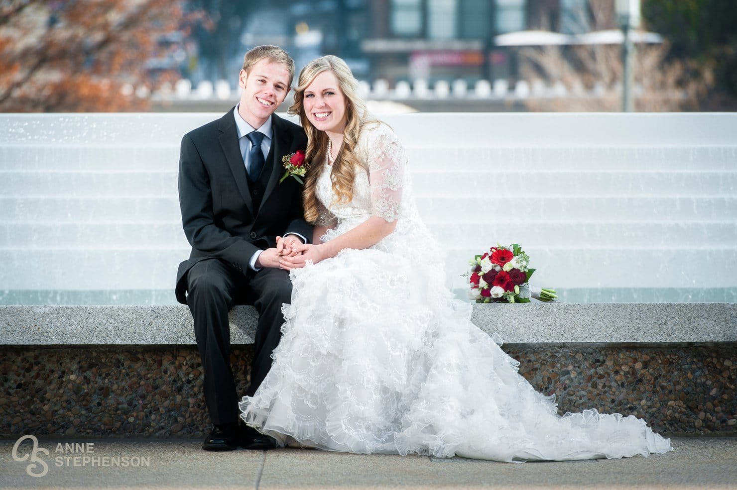 A recently sealed couple hold hands and sit in front of the fountain in winter at the SLC Temple.