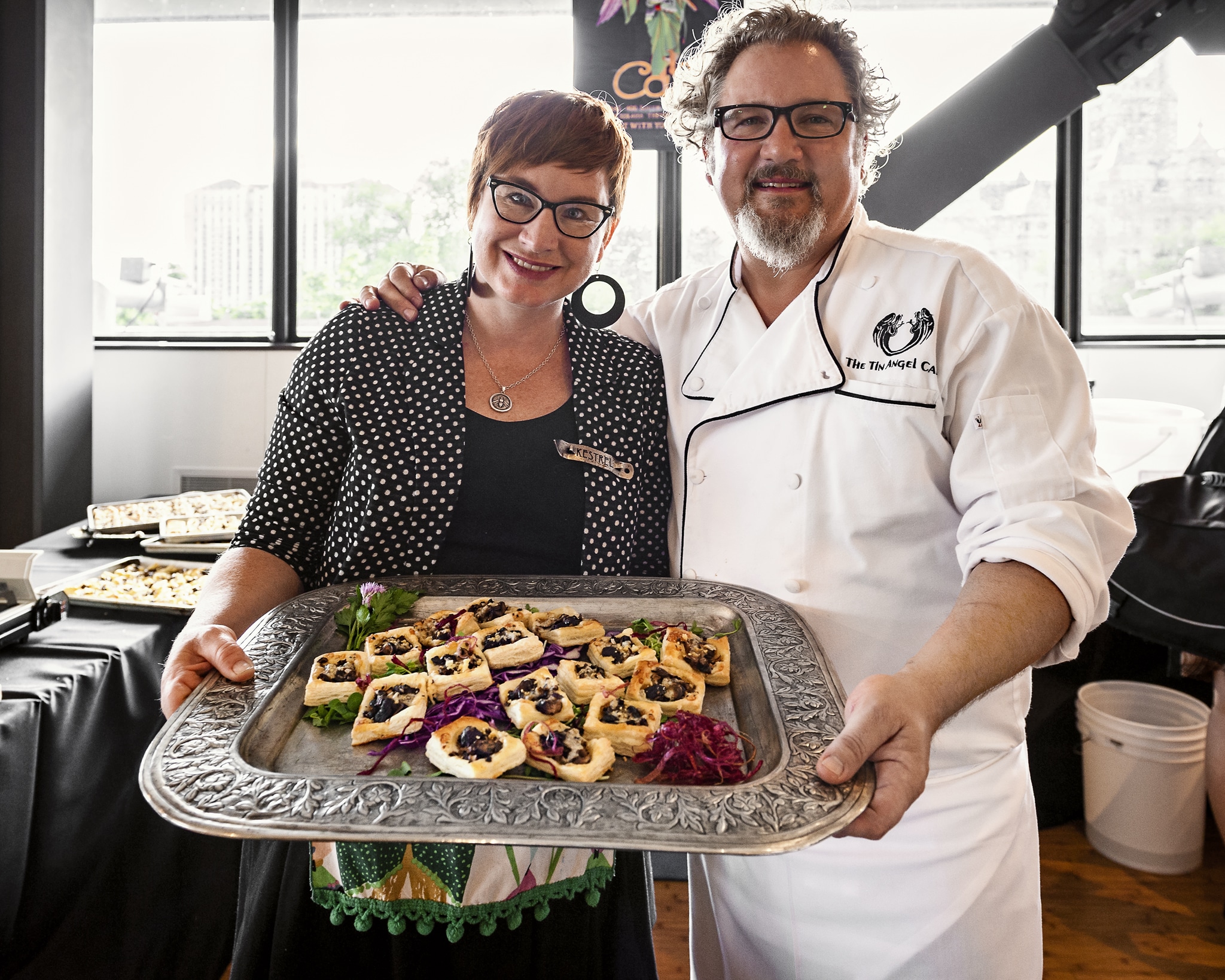 A man and woman from the Tin Angel hold a platter of savory tartlets of roasted crimini mushrooms and Irish cheddar cheese topped with hand grated truffles.