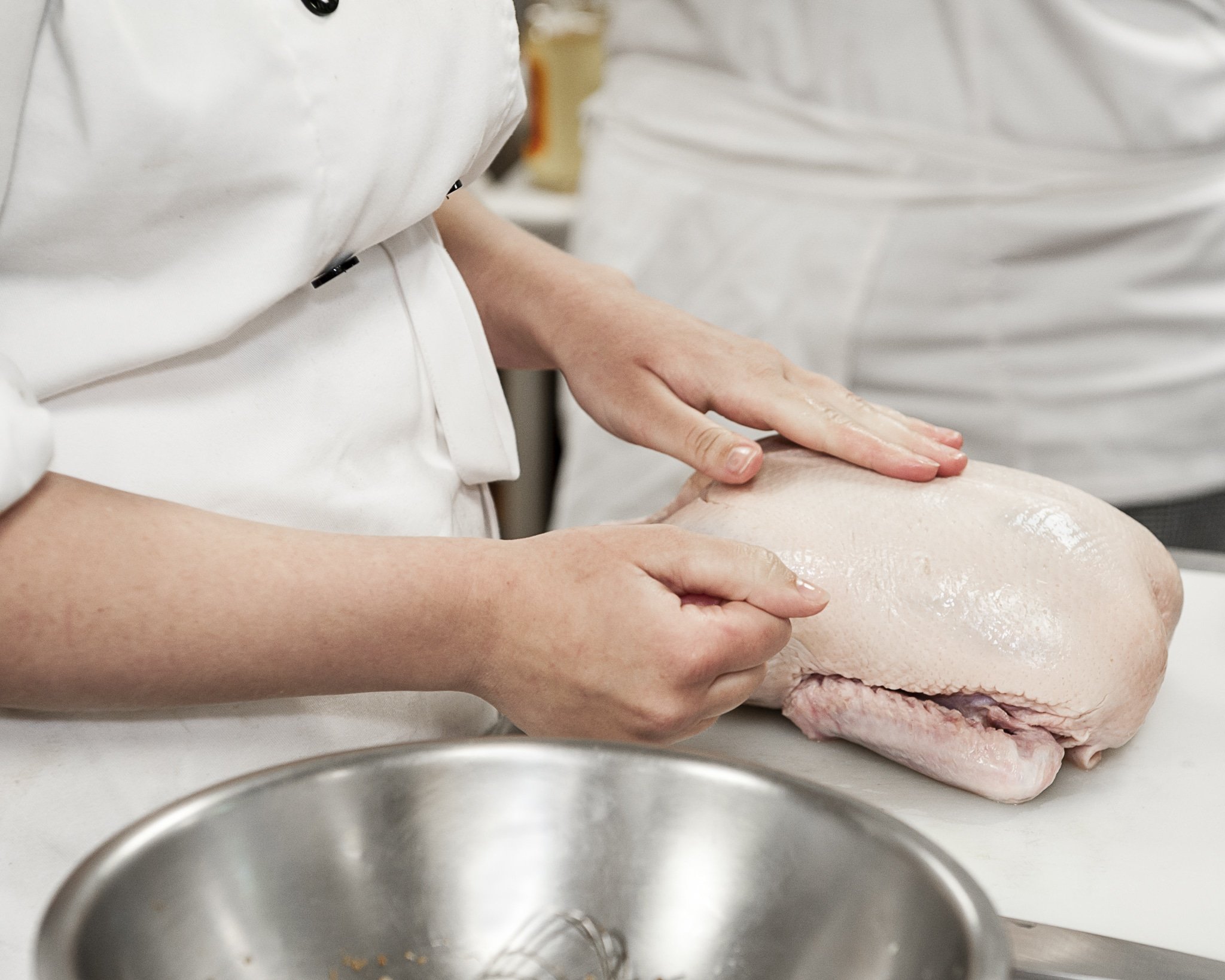 A culinary student begins to prepare a raw duck.