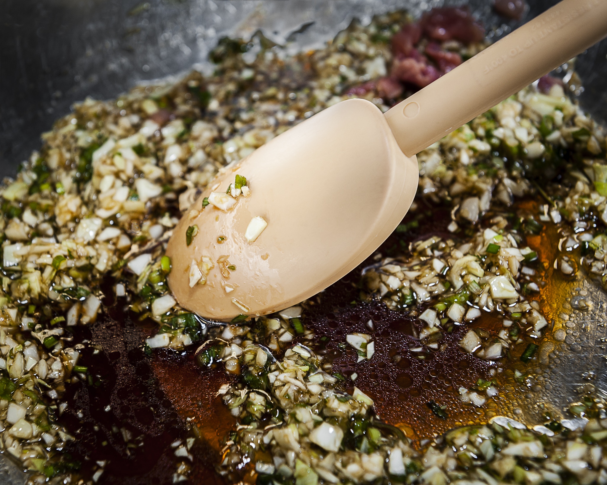 Close up of a rubber spatula in a bowl containing a mixture of soy sauce, onions, and spices.