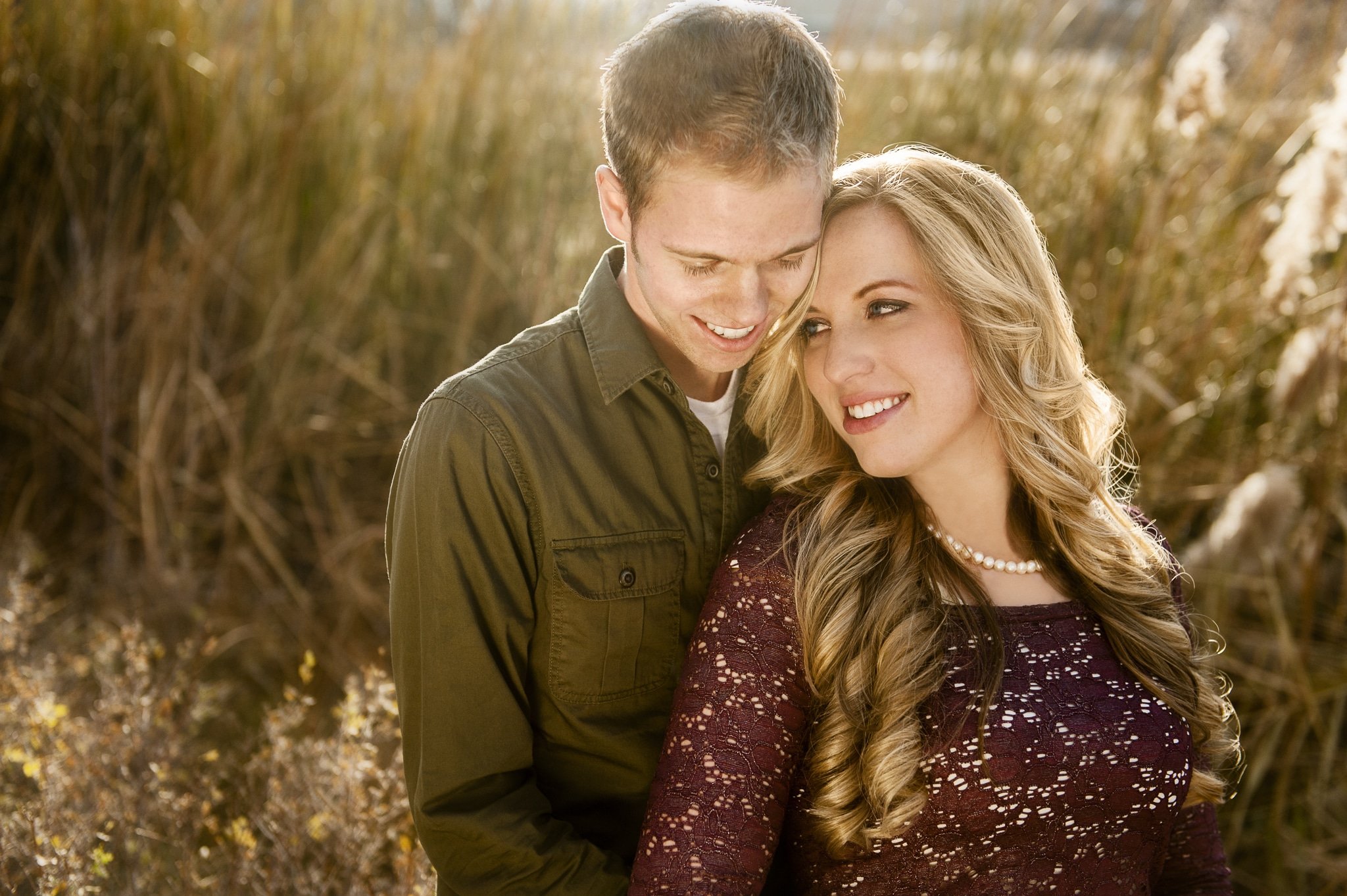 A woman leans her head back against her fiancé as they take a minute during their photo session in a backlit area with golden grasses.