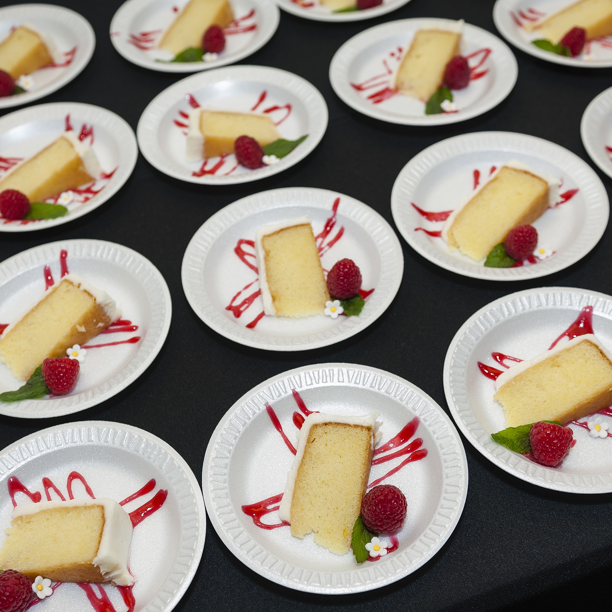 Several rows of plates containing lemon cake on top of raspberry drizzle.