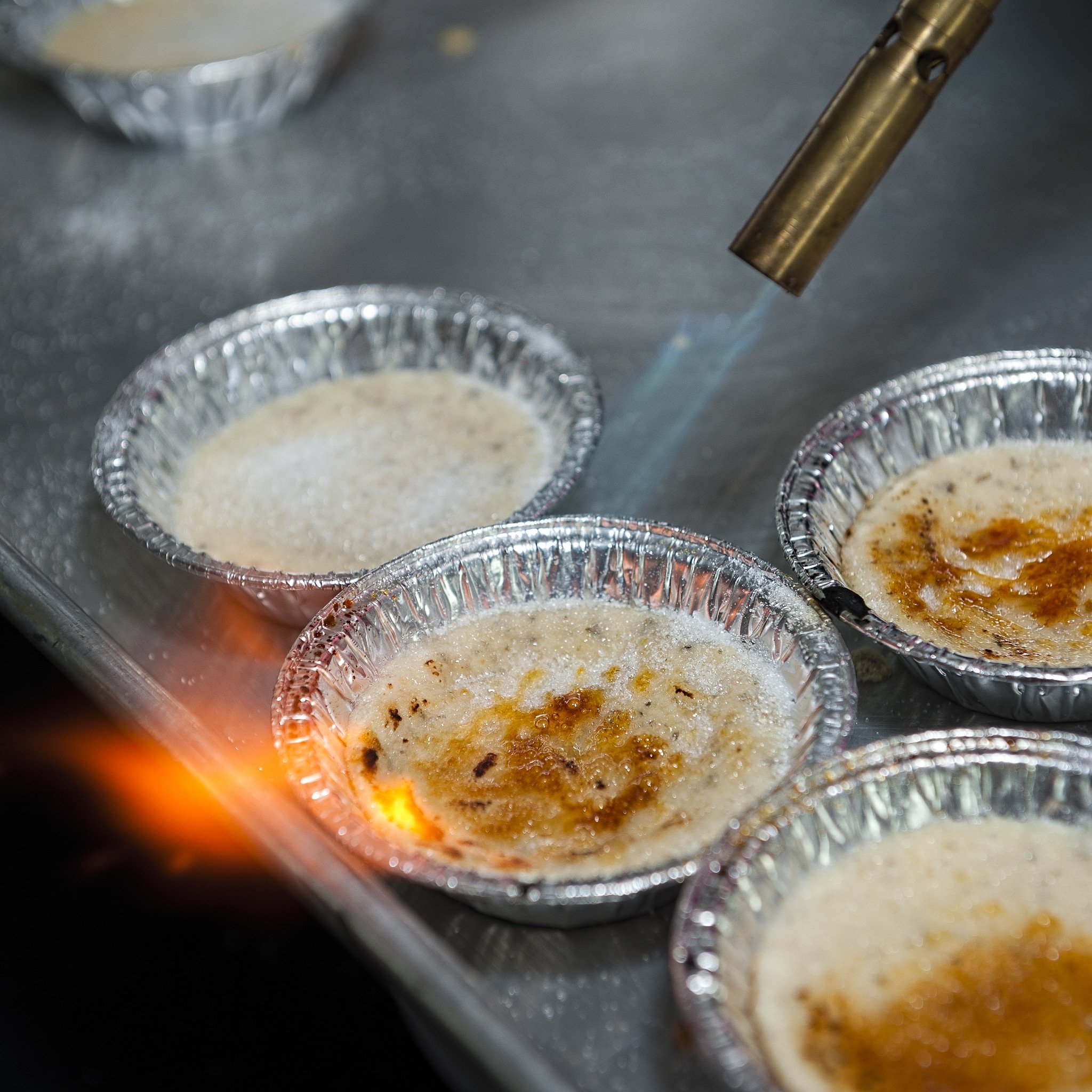 A flame caramelizes the top of sugar on top of a creme brulee.