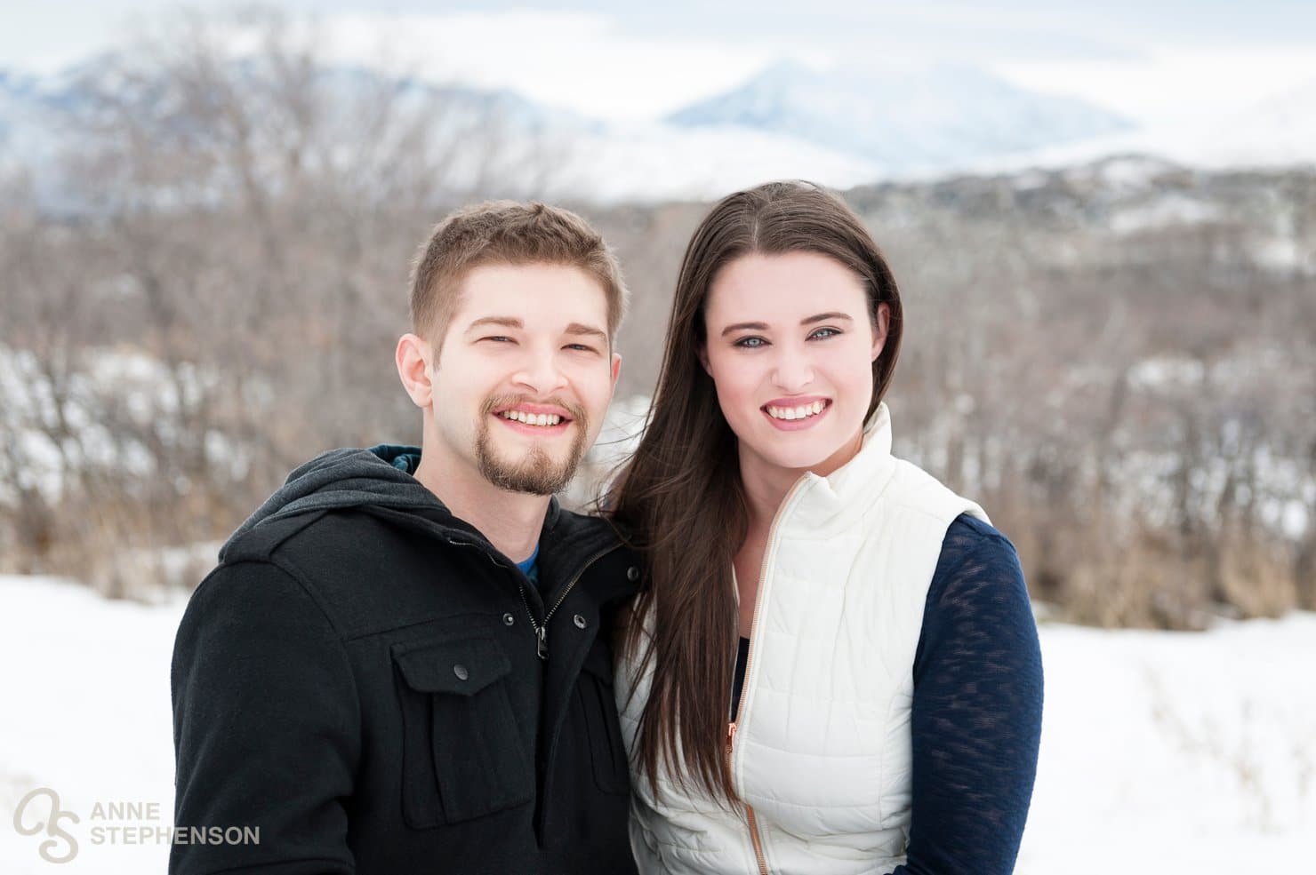 Winter engagement session traditional camera-facing photo of a man and woman with stormy mountains in the background.