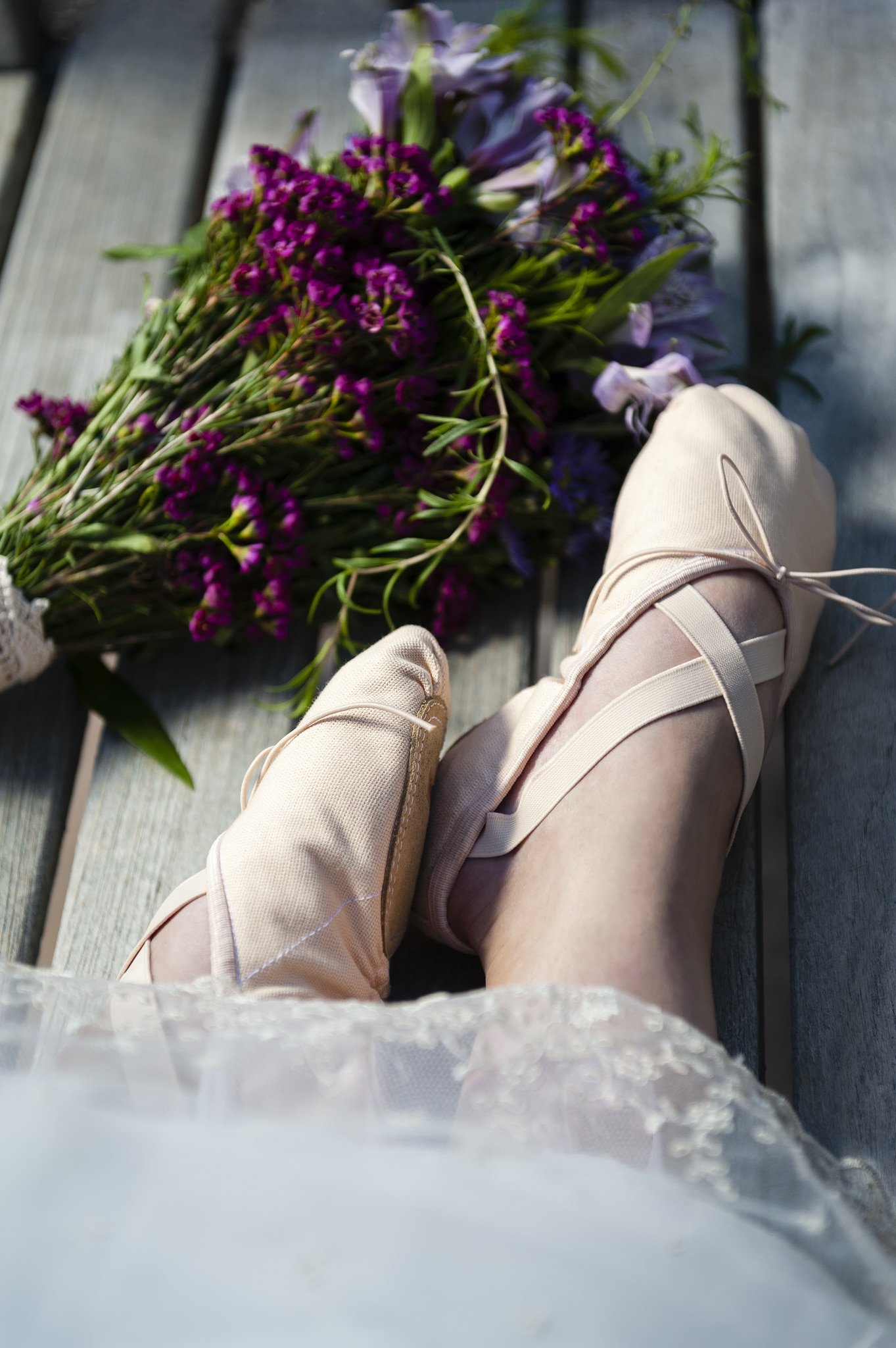 A close up of the wedding dress on a bride-to-be along with her ballet slippers and wildflower bouquet during her bridal photo session.