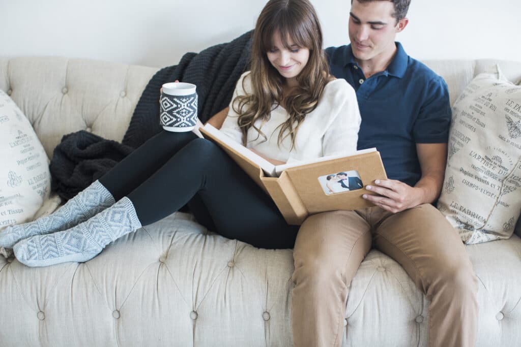 A married couple on a couch with a cup of coffee looks through their photo album and smiles at the memories.