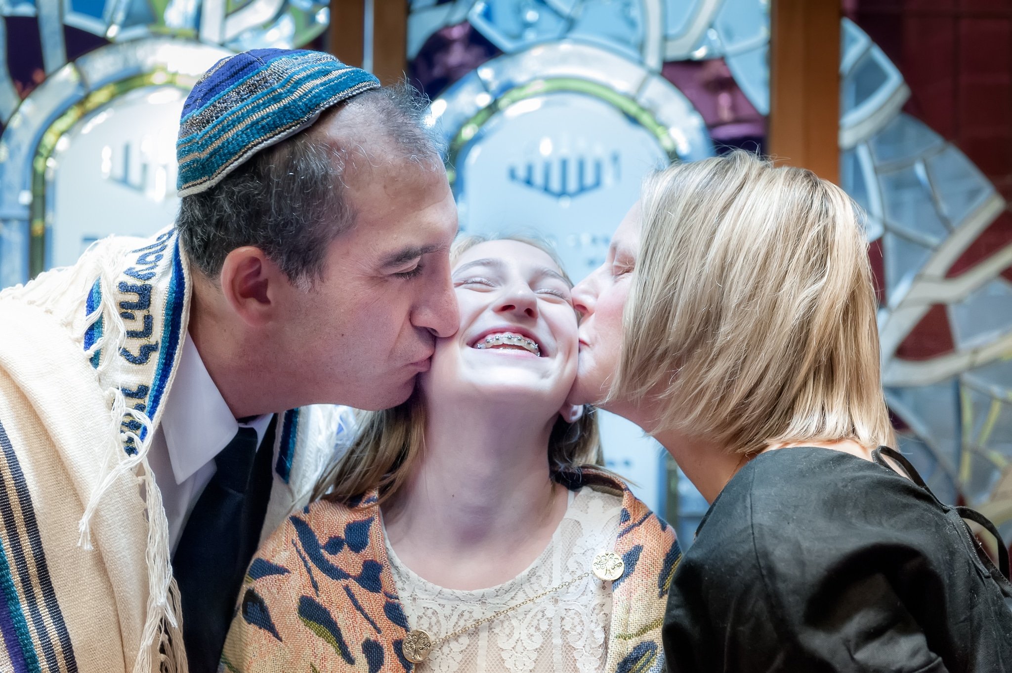 A mother and father kiss the cheeks of their daughter following her mitzvah practice.