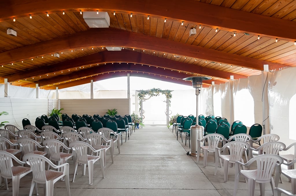 A wide angle view of the chairs set up for a wedding ceremony protected under a white tent.