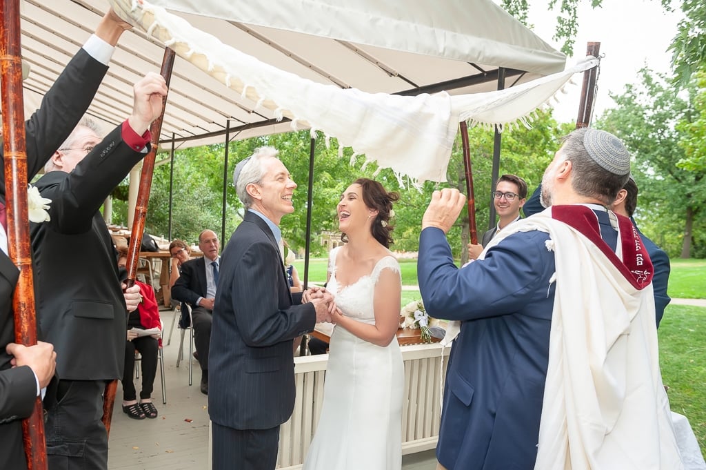 A bride and groom laugh under the chuppah during a Jewish wedding.