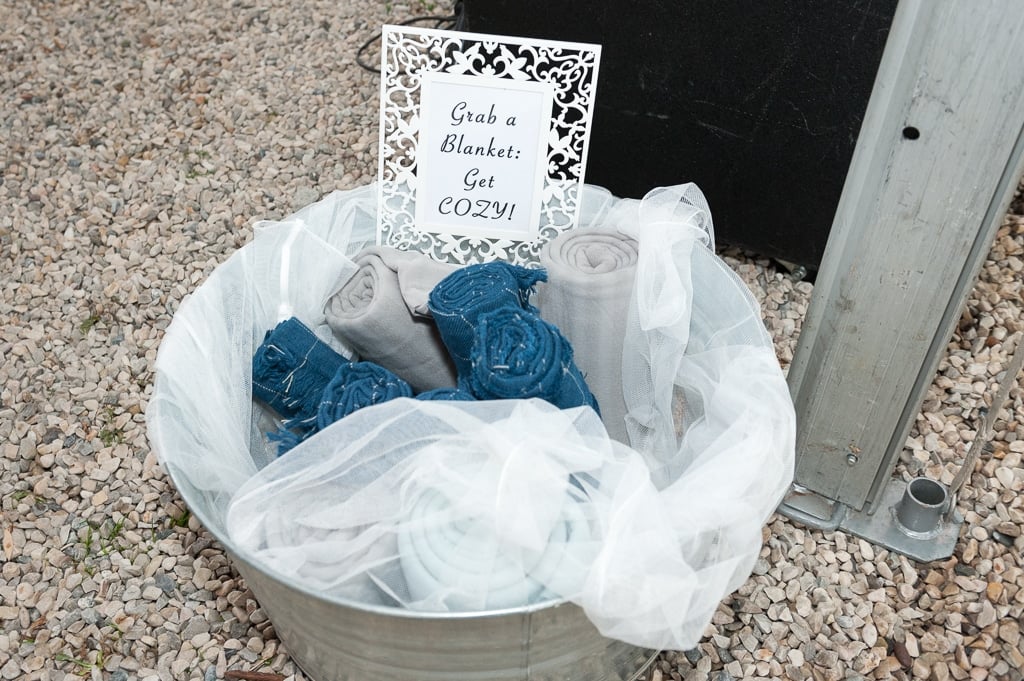 A large tin bucket decorated for a wedding holds blankets to keep guests warm during rainy day wedding photos.