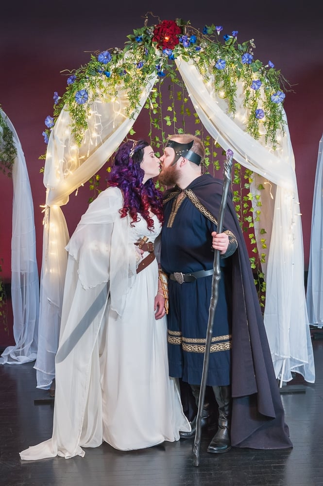 An offbeat bride and groom kiss underneath a canopy.