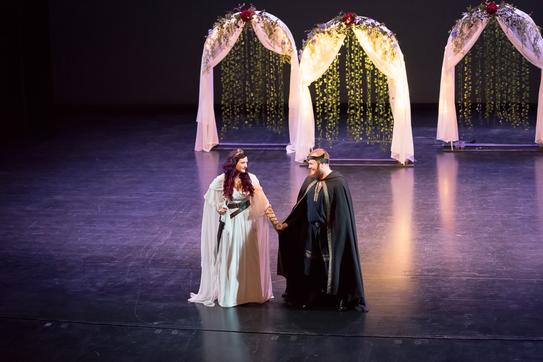 The bride and groom hold hands and walk across the stage at their wedding ceremony.