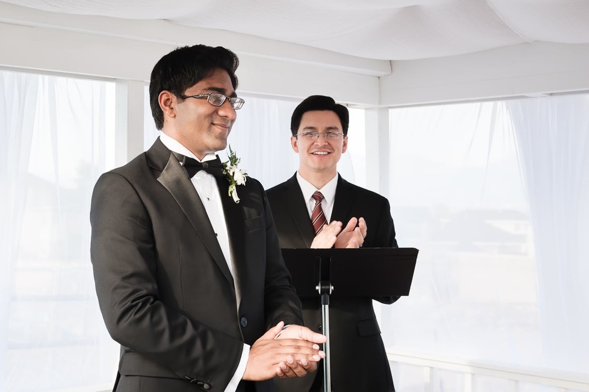 A groom beams with joy seeing his beautiful bride walk down the aisle in her wedding gown.