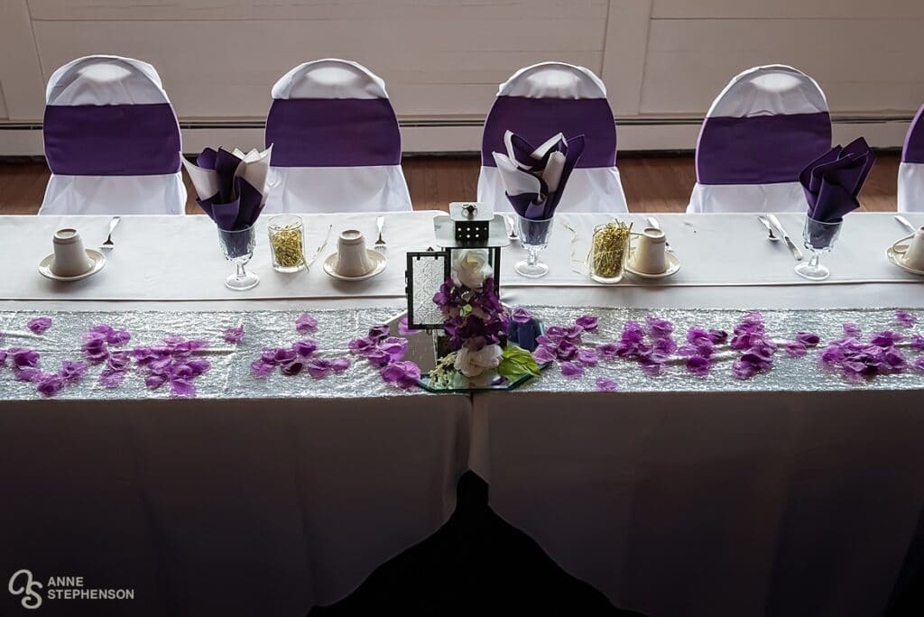 A table decorated in white and accented with purple linens and flower accents for a wedding celebration at Crystal Rose.