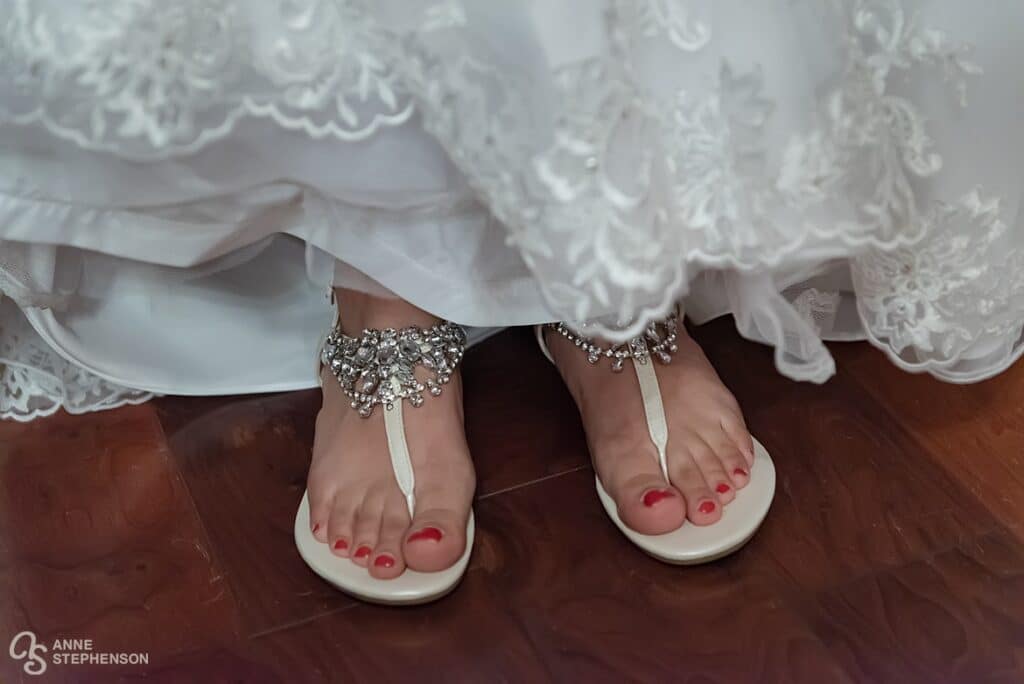 The bride shows her beautiful beaded sandals framed by the scalloped embroidered edge of her white wedding dress.