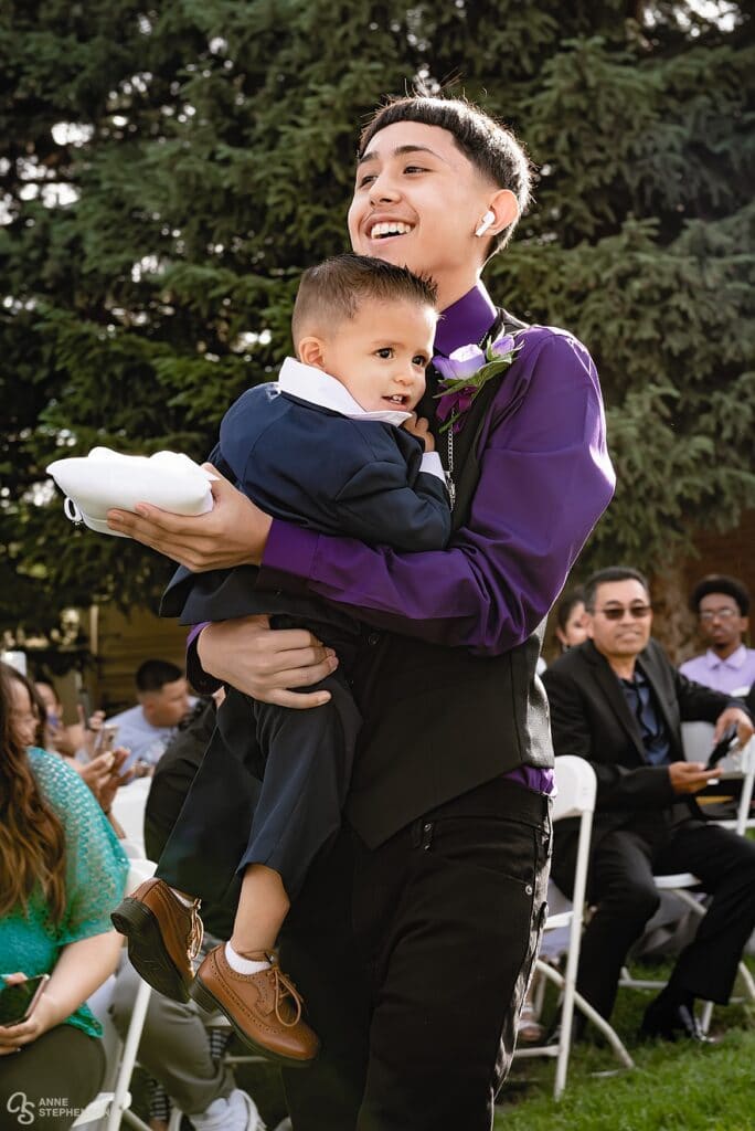 The ring bearer is carried up the aisle by his uncle.