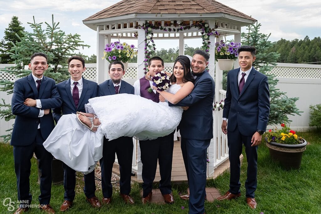 The five groomsmen lift up the bride and hold her for a photo.