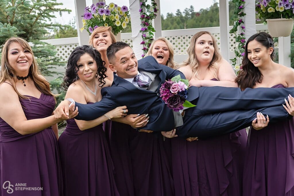 Five ladies of the wedding party do their best to lift the groom during the photo session.