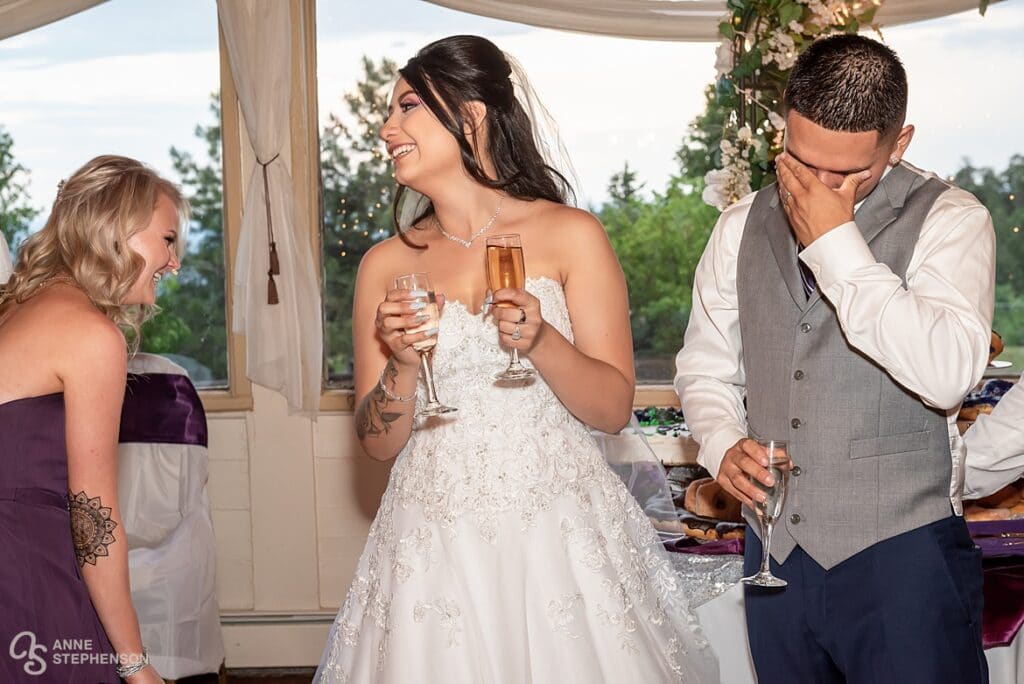 The bride laughs with her maid of honor as her husband covers her eyes during one of the toasts at the wedding.