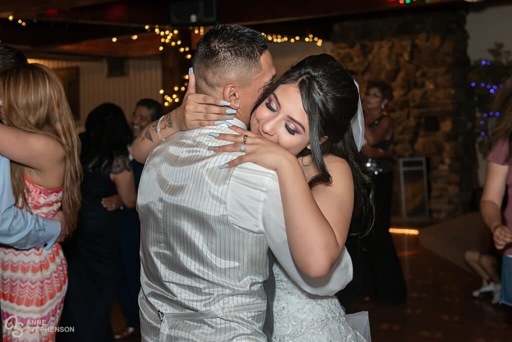 The bride hugs her groom tightly as they embrace during a dance together at their wedding reception.
