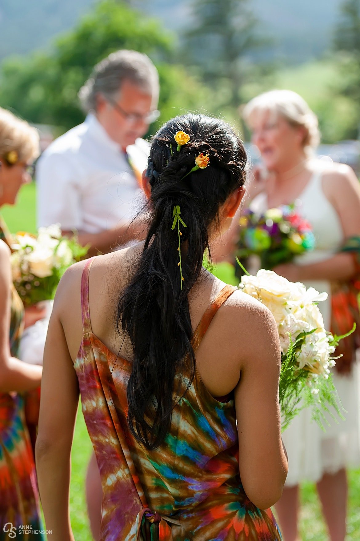 Back side view of the groom's daughter with pretty ribbons woven in her dark Asian hair and colorful tie-dye attire.