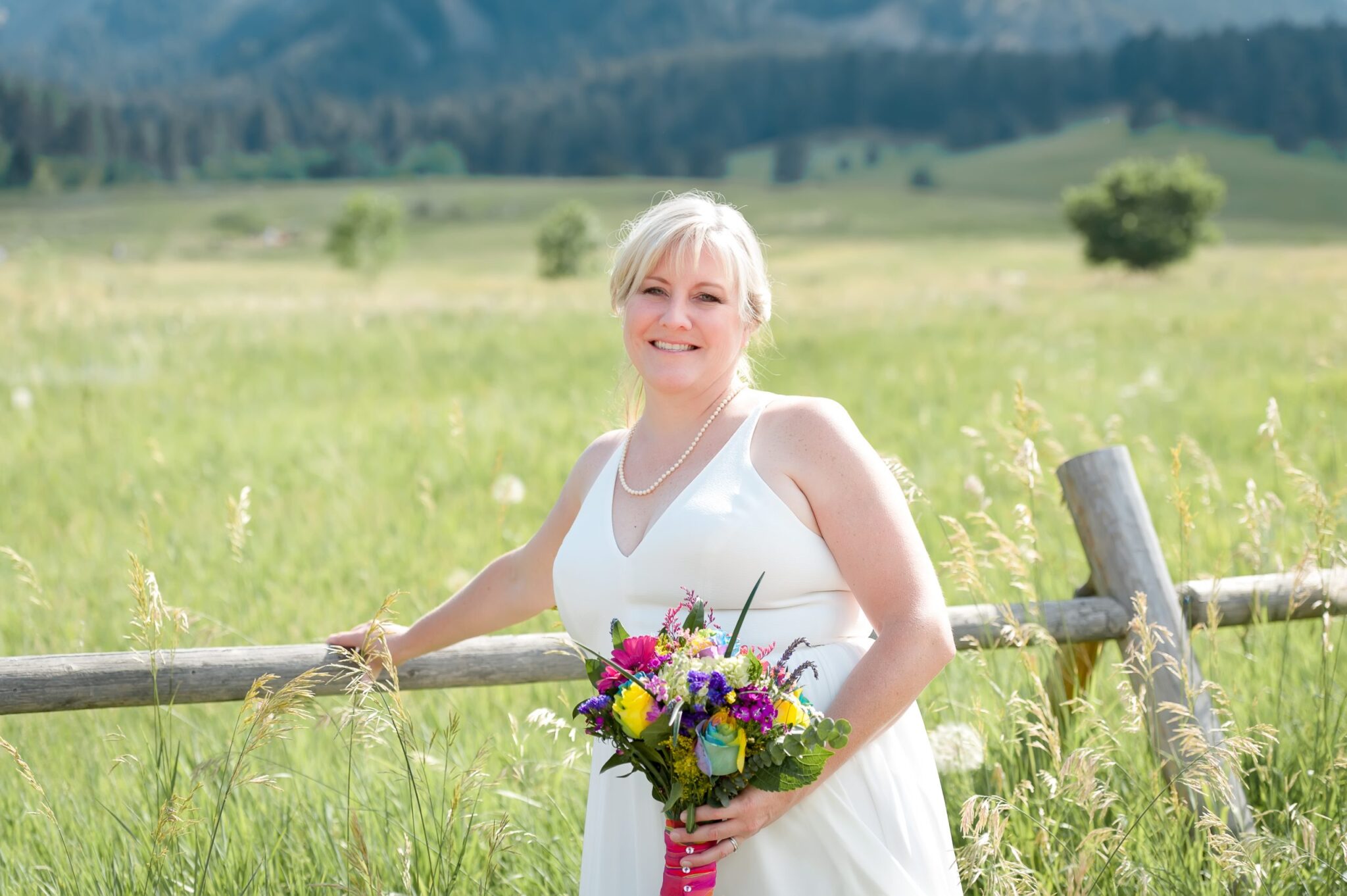 The bride in a white dress and brightly colored bouquet of vibrant flowers poses against a split rail fence at Chautauqua Park, Boulder, Colorado. 