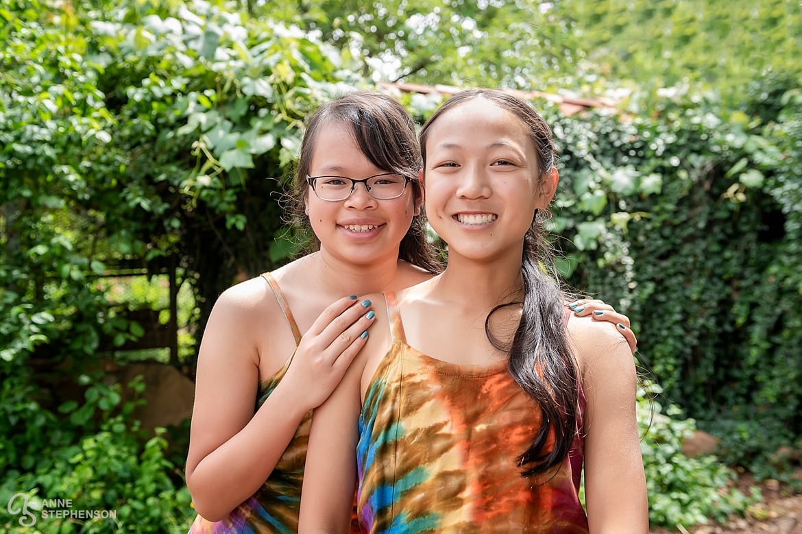 Two sisters in brightly colored tie-dye dresses in shades of orange, yellow, and green, pose for the camera on the father's wedding day.