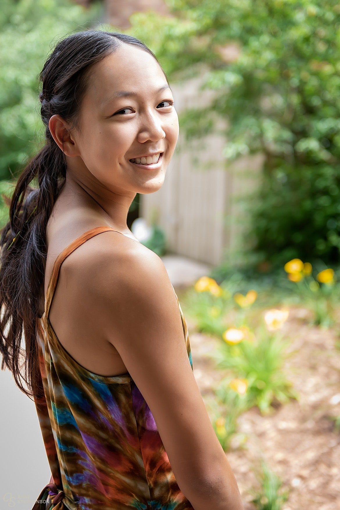 One of the groom's teenage daughters turns to look over her shoulder and smile broadly at the camera. She is wearing a tie-dye dress that matches her sister.