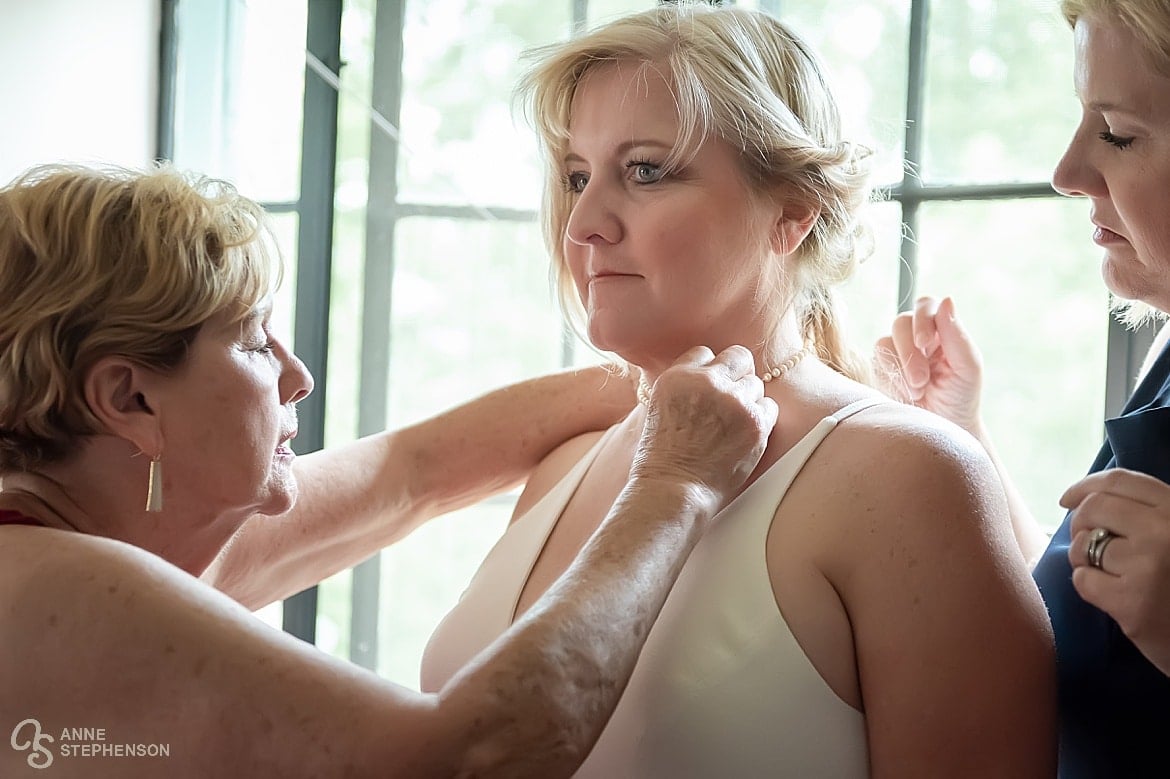 The mother of the bride secures a family pearl necklace  the only traditional item at this tie-dye wedding.