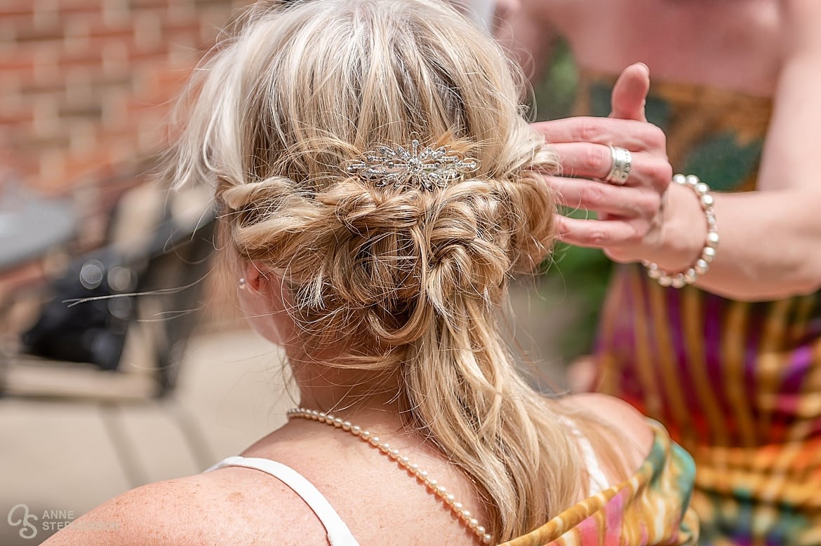 A friend of the bride and professional stylist uses her artistry to pin up the back of the brides hair and affix a comb with a single diamond.