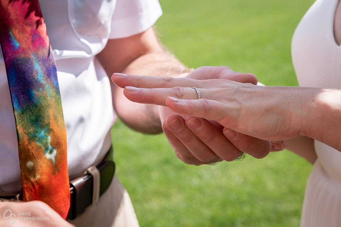 Close up of the bride's hand as the groom places the wedding ring on her finger.