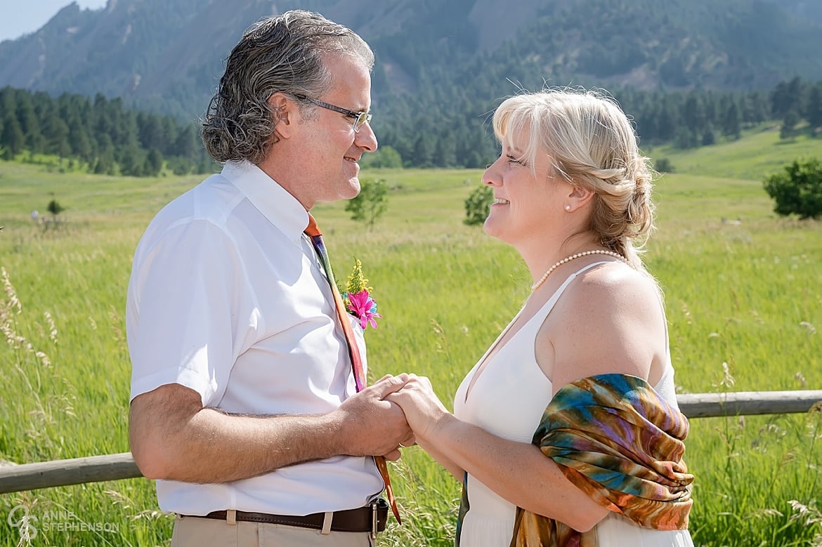 The bride and groom after their tie-dye wedding in Chautauqua Park pose in front of a split-rail fence with the Flatiron mountains in the background.