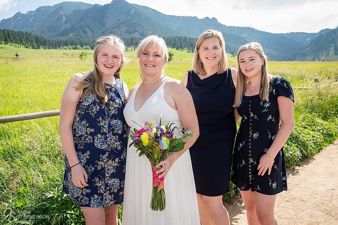 The bride with her sister and two  nieces along a fence and pathway at Chautauqua Park on a sunny day with the Flatirons in the background.