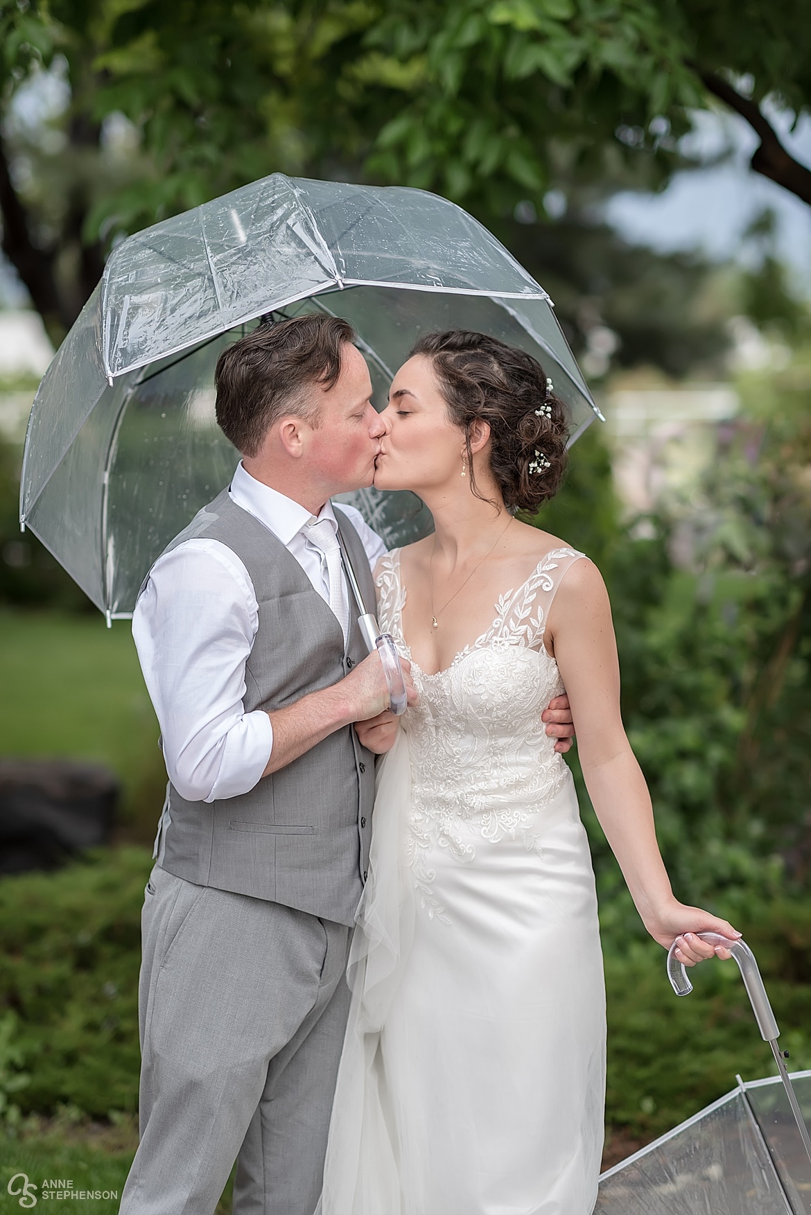 A bride and groom share a kiss under a clear plastic umbrella after their spring wedding ceremony.