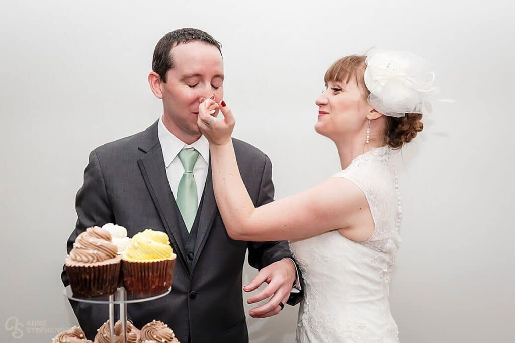 The bride playfully puts a dollop of frosting on the nose of the groom during the cake cutting.