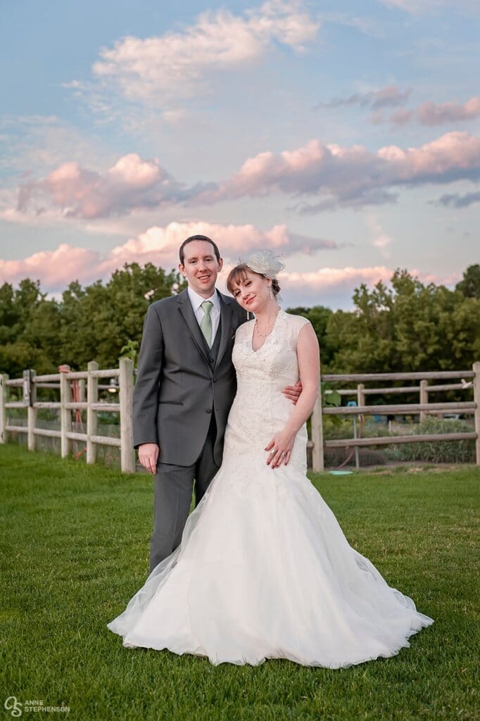 Bride and groom during sunset with pink clouds and the grassy areas of Heritage Lakewood in the background.