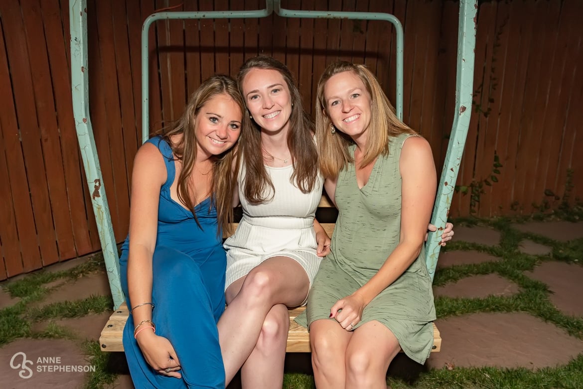 Three best women friends sit on a ski chair in a friend's backyard.