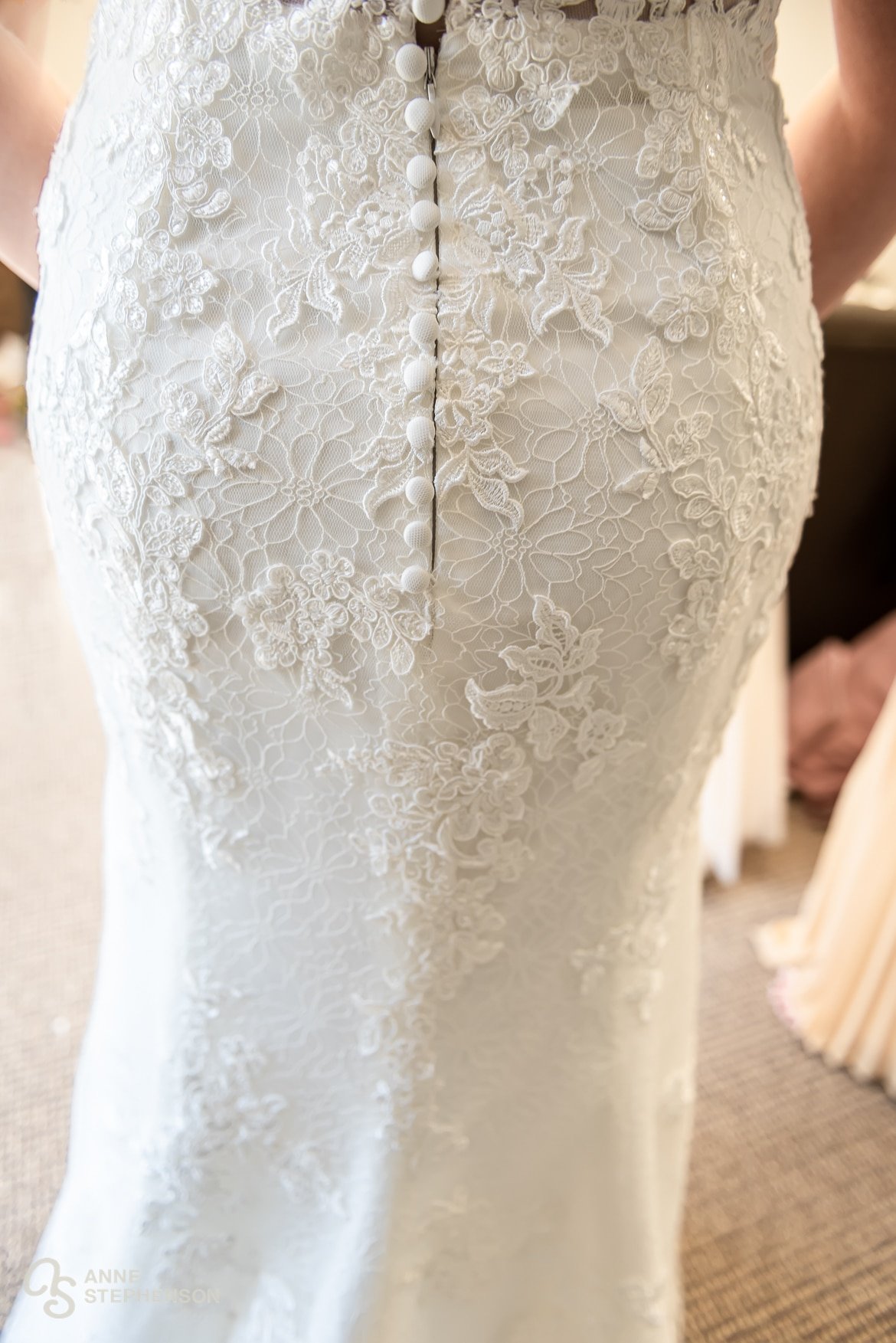 A close up view of the embroidery, lace, and buttons on the back side of the bride's wedding dress.