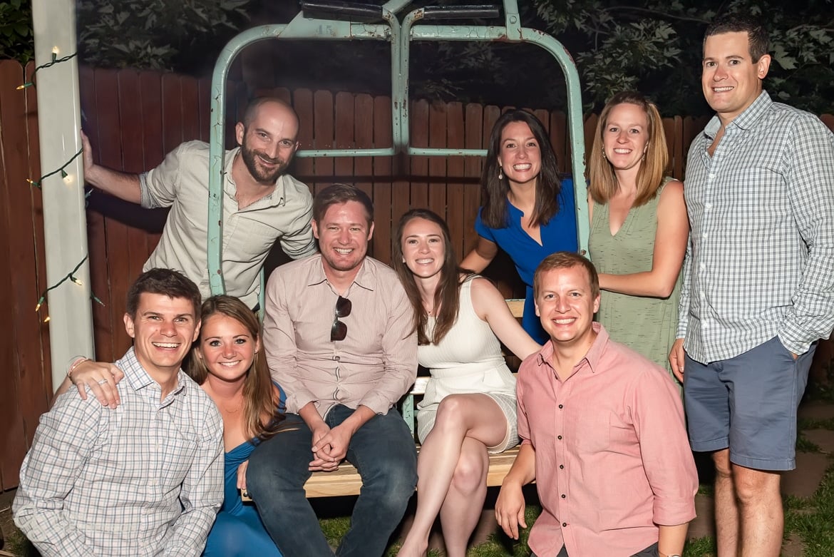 A group photo of friends sit on a  historic chair lift in a friend's backyard where several of their wedding proposals took place.