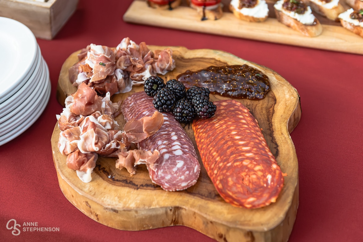 A charcuterie plate on a table with a red tablecloth at an outdoor wedding reception celebration.