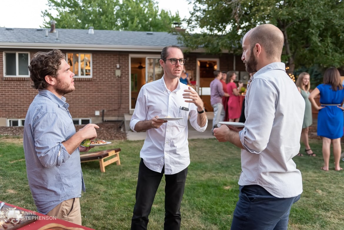 A man makes a point by using a hand gesture during party conversation at a backyard wedding celebration.