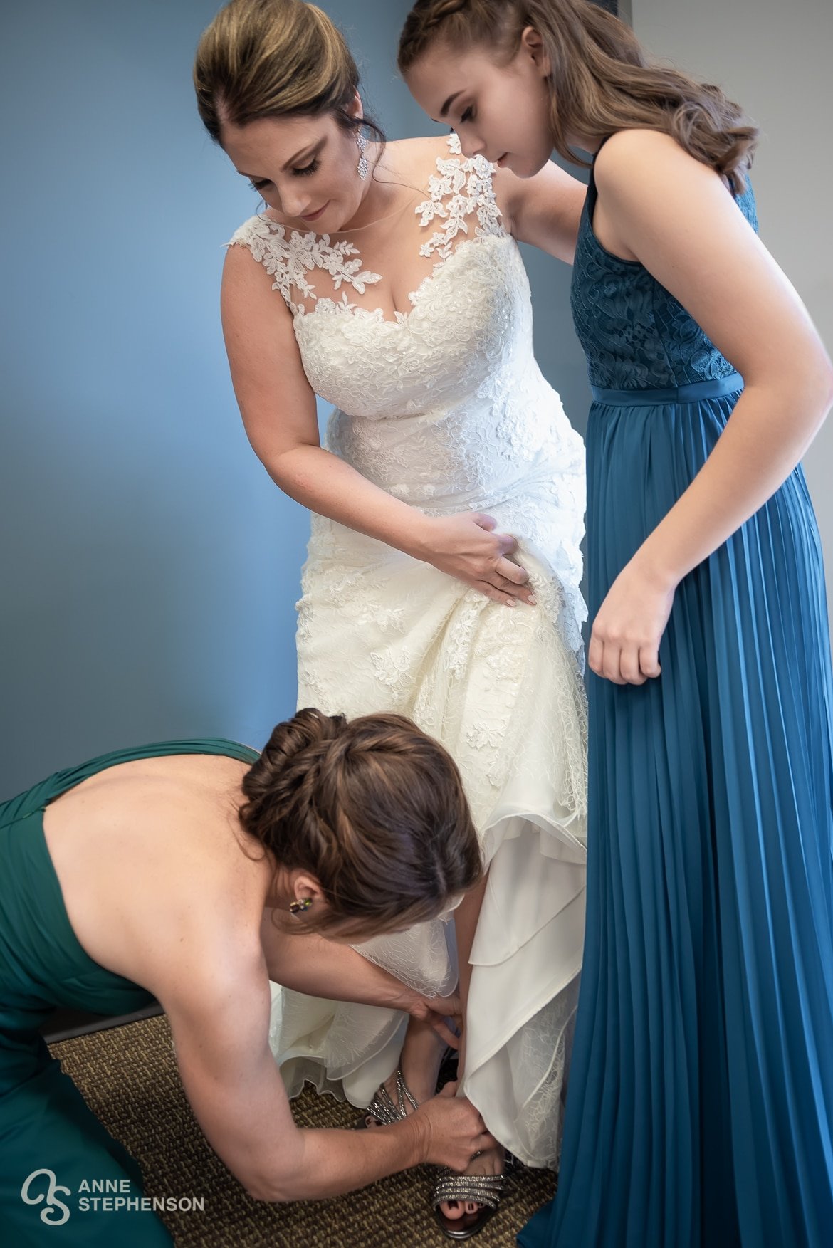 One of the bride's attendants helps with fastening her sandals.