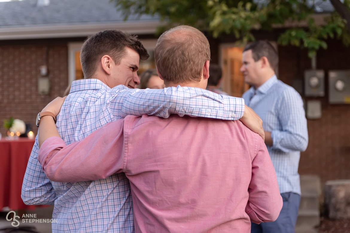 Two male friends walk with arms wrapped around each other's shoulders.