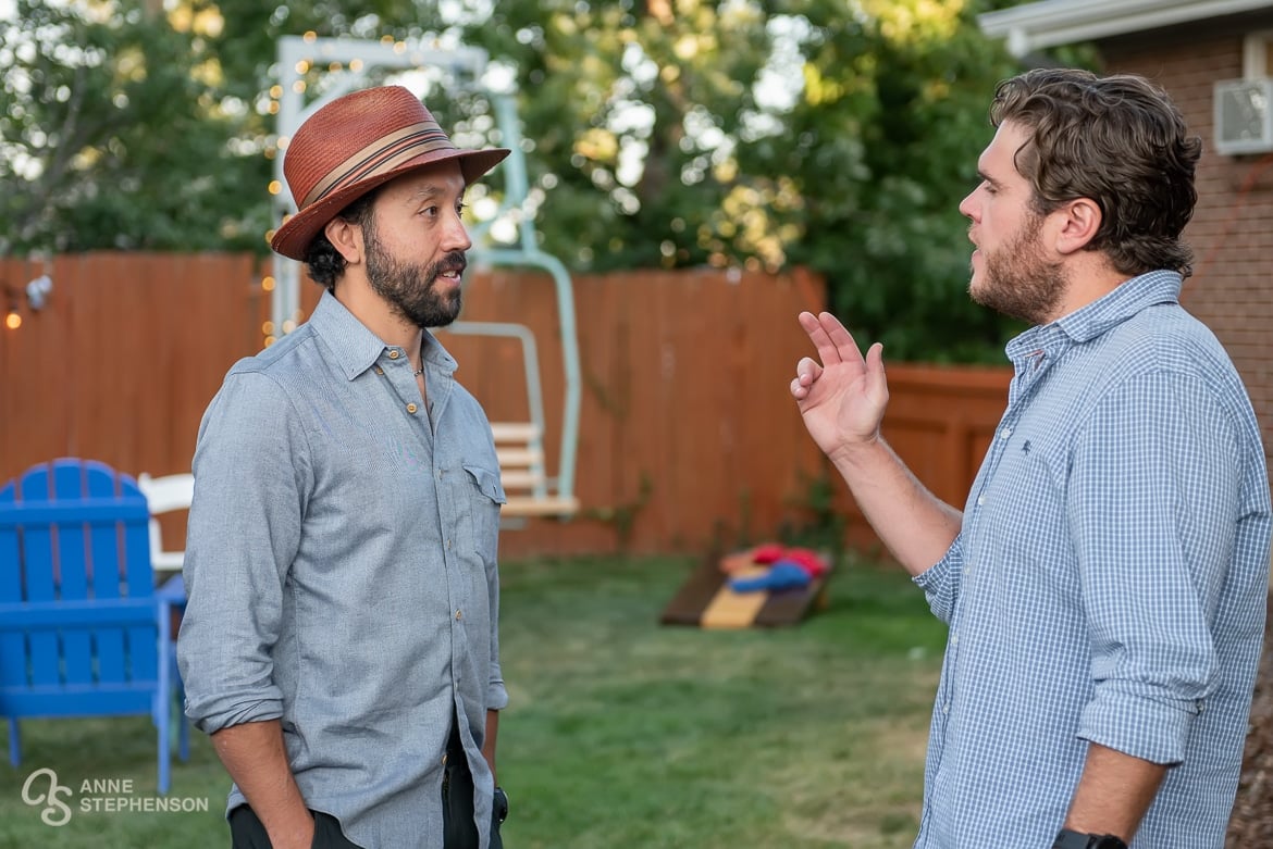 Two men engage in lively conversation at a backyard party.