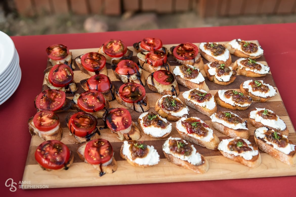 A cutting board filled with bruschetta appetizers topped with cheese and cherry tomatoes.